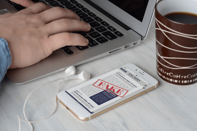 איש עסקים על המקלדת עם כוס קפה וחדשות מזויפות דיגיטליות בסמארטפון